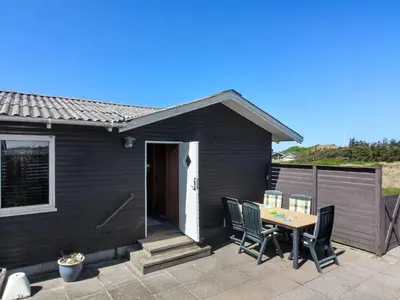 a black house with a table and chairs on a patio at Holiday Home Mira - 375m from the sea by Interhome in Løkken