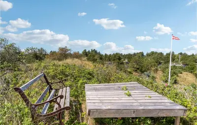 a wooden bench sitting in a field with a flag at Nice Home In Blokhus With Kitchen in Blokhus