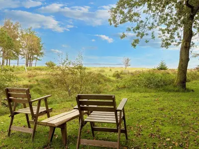two wooden chairs and a bench in a field at 8 person holiday home in Thyholm-By Traum in Thyholm