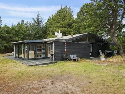 a small black cabin with a deck in a field at Holiday Home Velika - 1-2km from the sea by Interhome in Thisted