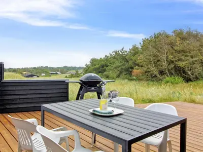 a picnic table with white chairs and a grill on a deck at Holiday Home Alma - 500m from the sea by Interhome in Løkken