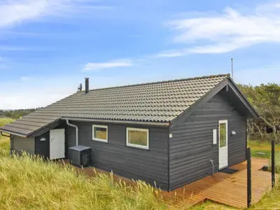 a black house with a wooden deck in a field at Holiday Home Alma - 500m from the sea by Interhome in Løkken