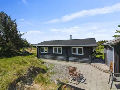 a black cottage with two chairs on a patio at Holiday Home Sampo - 400m from the sea by Interhome in Løkken