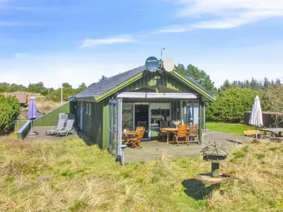 a green building with a table and chairs in a field at Holiday Home Gerasim - 1km from the sea by Interhome in Saltum