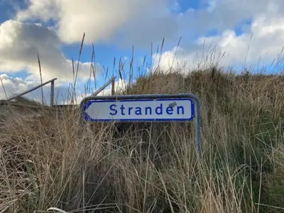a blue and white street sign sitting in the grass at Agger Beach Apartment in Vestervig
