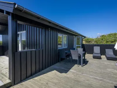 a black house with a deck with chairs and a table at Holiday Home Efra - 400m from the sea by Interhome in Saltum