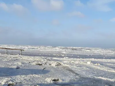a snow covered beach with a bench and the ocean at 4 star holiday home in Blokhus-By Traum in Blokhus