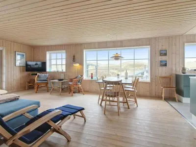 a living room with a table and chairs and a kitchen at Holiday Home Merina - 150m from the sea by Interhome in Løkken