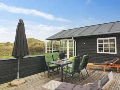 a deck with a table and chairs and an umbrella at Holiday Home Merina - 150m from the sea by Interhome in Løkken