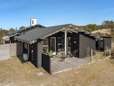 a black house with a deck on a hill at Holiday Home Annrike - 400m from the sea by Interhome in Saltum