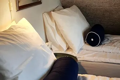 a person is sitting on a bed with pillows at Centralt by hus Blokhus-Hune til 10 pers privat Gårdhave in Blokhus