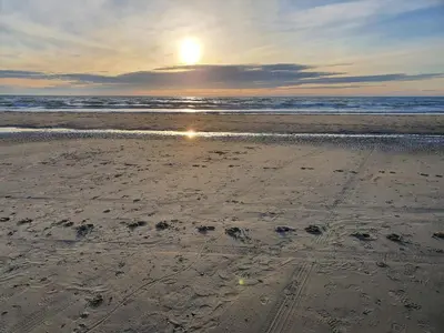 a beach with the sun setting over the ocean at Tranquil Beach Retreat - By Traum Ferienwohnungen in Løkken
