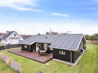 a black house with a deck in a yard at Holiday Home Svante - 600m from the sea by Interhome in Blokhus