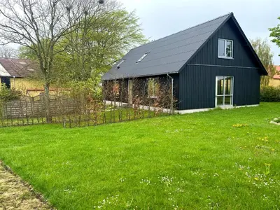 a black barn in a field of green grass at Volstrup Ferieboliger in Stenild