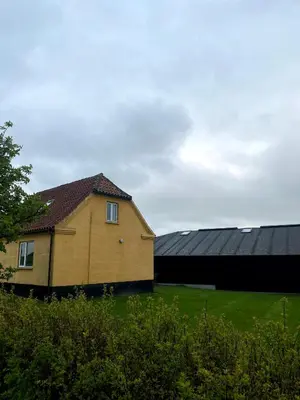a yellow house with black roofs in a field at Volstrup Ferieboliger in Stenild