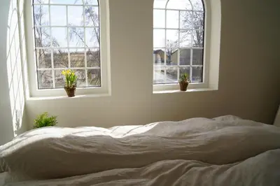 an unmade bed in a bedroom with two windows at Volstrup Ferieboliger in Stenild
