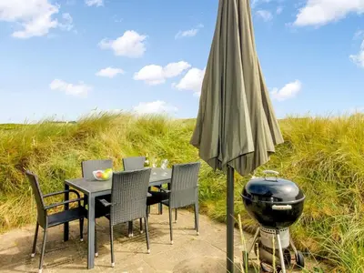 a grill and an umbrella next to a table and chairs at Holiday Home Pinja - 400m from the sea by Interhome in Løkken