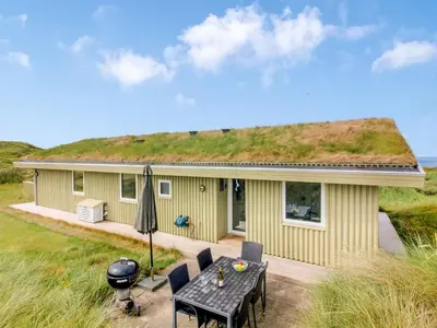 a yellow house with a grass roof with a table at Holiday Home Pinja - 400m from the sea by Interhome in Løkken