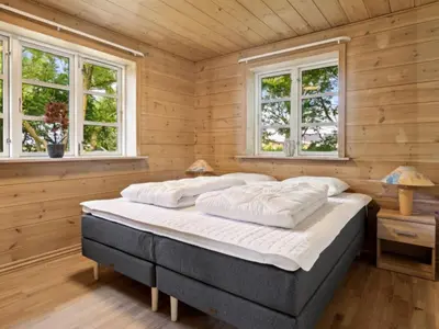 a bed in a wooden room with two windows at Holiday Home Månviva - 150m to the fjord by Interhome in Redsted