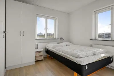 a white bedroom with a bed and two windows at Pool house with beautiful view by the sea - SJ650 in Lemvig