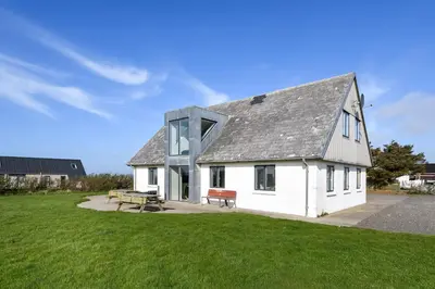 a white house with a gray roof on a grass field at Pool house with beautiful view by the sea - SJ650 in Lemvig
