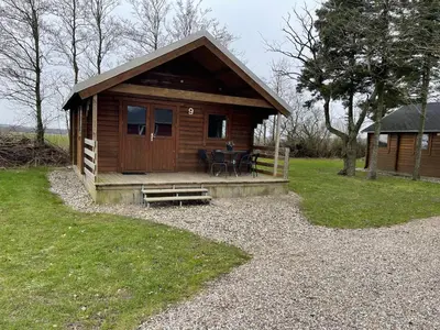 a small wooden cabin with a table and a porch at Himmerland camping & Feriecenter in Års