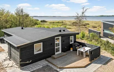 a black tiny house with a deck next to a lake at 2 Bedroom Awesome Home In Højslev in Højslev