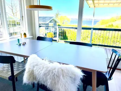 a dining room table with chairs and a large window at Dejligt sommerhus med udsigt over fjorden in Løgstrup