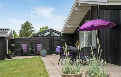 a patio with a table and purple chairs and an umbrella at 4 Bedroom Beautiful Home In Blokhus in Blokhus