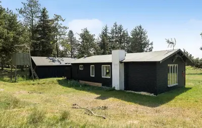 a small black house in a field with trees at Røgegård Hjortehytten in Fjerritslev
