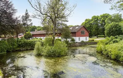 a river in front of a red barn and a house at Lejl 3 in Brovst