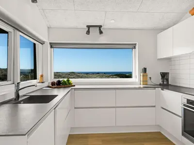 a kitchen with white cabinets and a large window at Holiday Home Carit - 450m from the sea by Interhome in Løkken