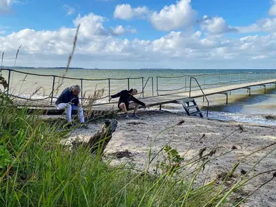 two people sitting on a bench on the beach at 5 person holiday home in Roslev-By Traum in Roslev