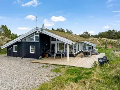 a black house with a roof on a wooden deck at Holiday Home Annlisa - 1km from the sea by Interhome in Blokhus