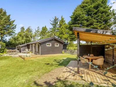 a backyard with a wooden table and a cabin at Holiday Home Jenvold - 1-5km from the sea by Interhome in Blokhus