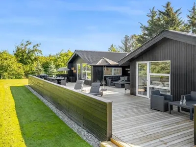 a wooden deck with chairs and tables on a house at Holiday Home Ema - 1-9km from the sea by Interhome in Saltum