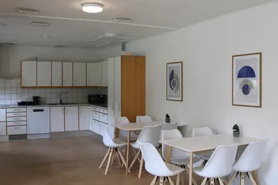 a room with two tables and white chairs and a kitchen at Hotel Traneparken in Nykøbing Mors