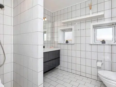 a white tiled bathroom with a sink and a toilet at 4 star holiday home in Blokhus-By Traum in Blokhus