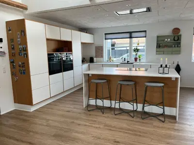 a kitchen with white cabinets and a island with bar stools at Hus tæt ved havn og strand in Thyborøn