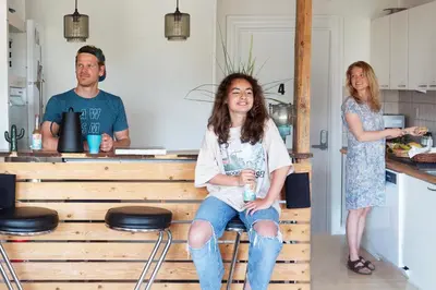 a girl sitting on a bench in a kitchen with two people at Stone MT Garden Pod in Snedsted