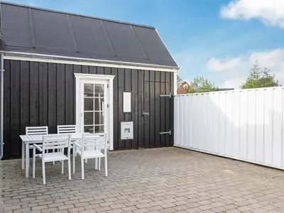a patio with a table and chairs next to a black building at 6 person holiday home in Blokhus-By Traum in Blokhus