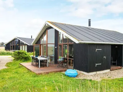 a black house with a deck and a table at 8 person holiday home in Ulfborg in Thorsminde
