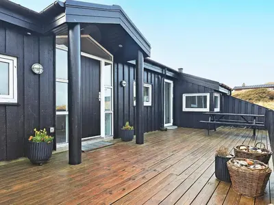 a black house with a wooden deck with potted plants at Luxury Beachfront Retreat - By Traum Ferienwohnungen in Rødhus