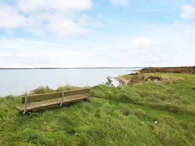 a bench sitting on the grass near a body of water at Seaside Rustic Retreat - By Traum Ferienwohnungen in Flovtrup