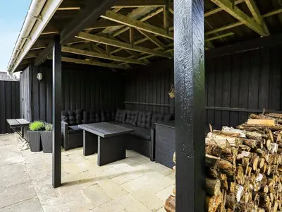a covered patio with a table and chairs and logs at 6 person holiday home in Blokhus-By Traum in Blokhus