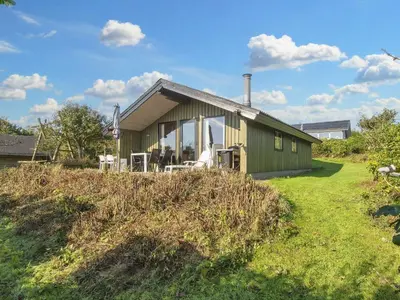 a green house on a grassy hill next to a house at 7 person holiday home in Lemvig-By Traum in Lemvig