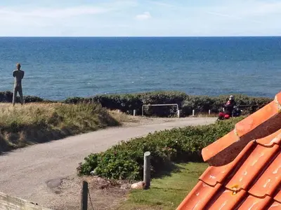 a man standing next to a bench overlooking the ocean at 4 person holiday home in Lemvig-By Traum in Trans