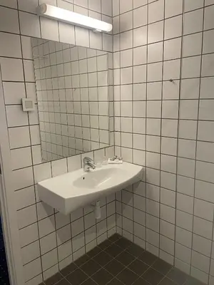 a white tiled bathroom with a sink and a mirror at Hotel Tante in Lemvig