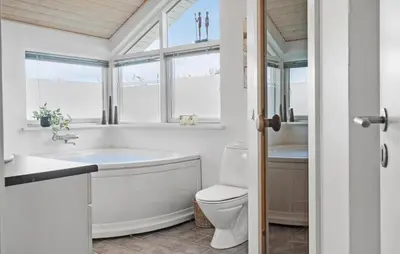 a bathroom with a tub and a toilet and windows at Cozy Home In Lemvig With Sauna in Lemvig