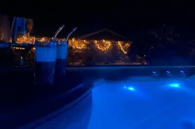 a glass of blue liquid sitting next to a swimming pool at night at Rækkehus tæt på skov, sø og by in Viborg